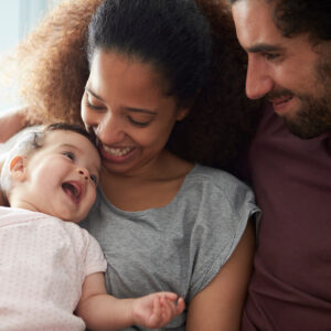 Parents Sitting On Sofa Cuddling Baby Daughter At Home